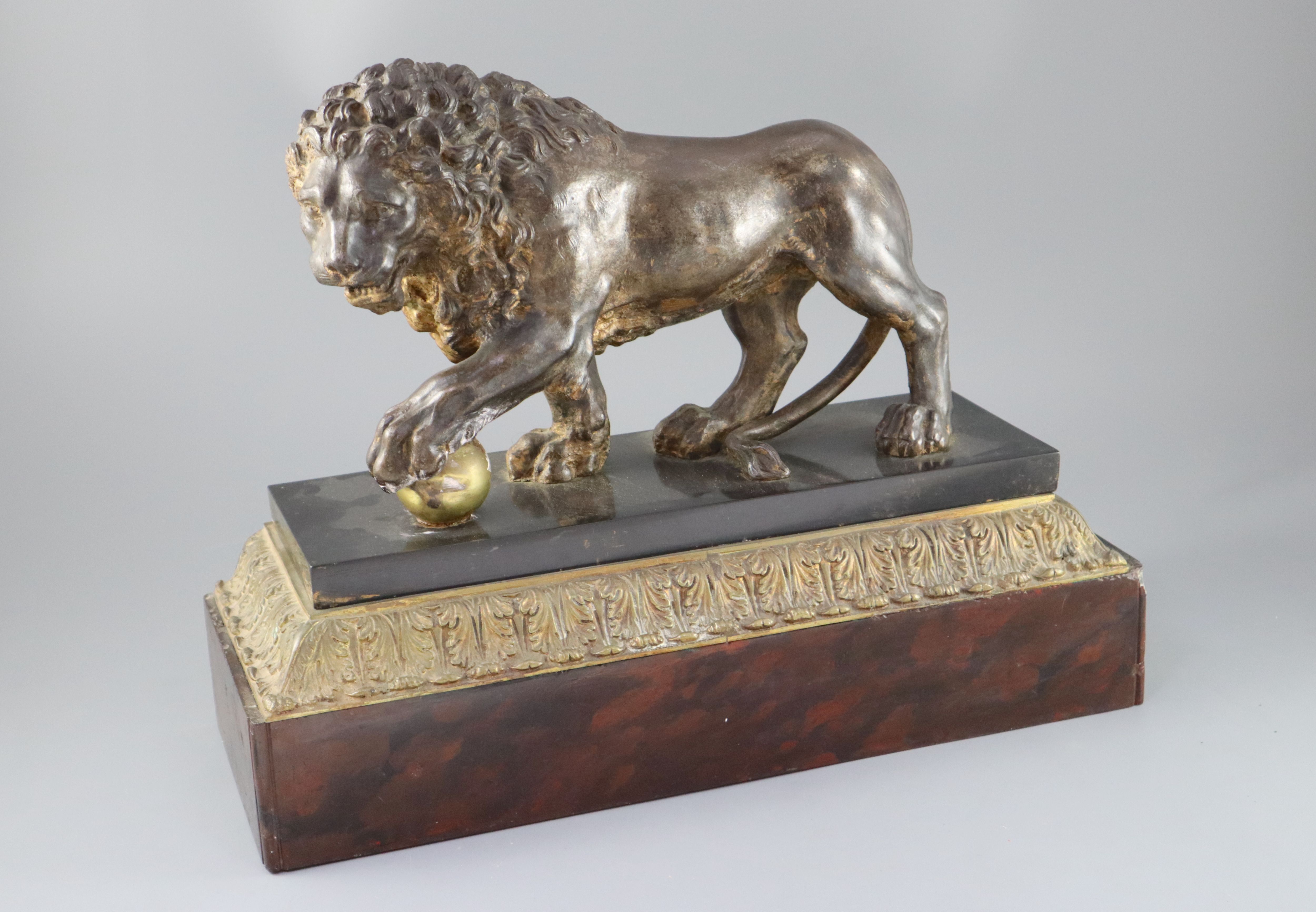 An early 19th century cast iron model of a lion standing with its foot upon a brass ball, width 15in. height 9.25in.